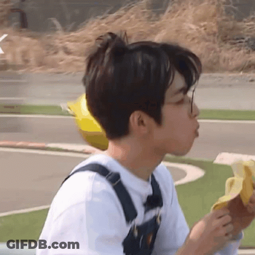 A Young Man Wearing Overalls Is Eating A Banana GIF