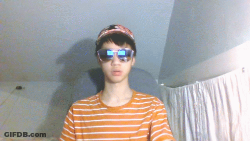 A Young Man Wearing Sunglasses And A Baseball Cap Looks At The Camera GIF