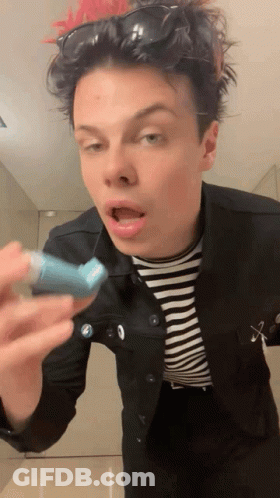 A Young Man Wearing Sunglasses And A Striped Shirt Is Holding A Blue Inhaler In His Hand GIF