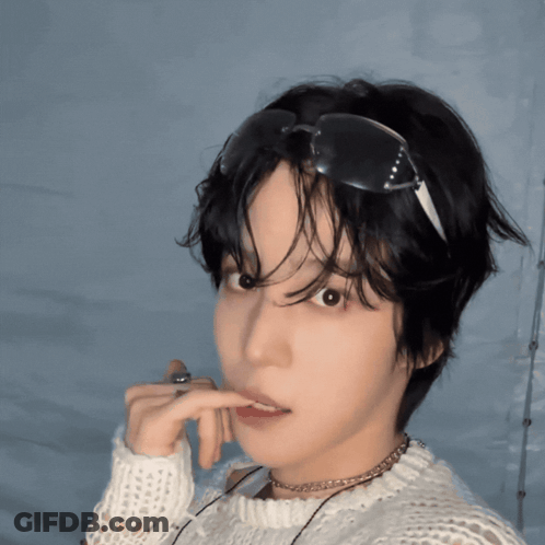 A Young Man Wearing Sunglasses And A White Sweater Looks At The Camera GIF