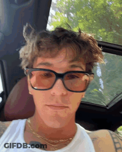 A Young Man Wearing Sunglasses And A White Tank Top Is Sitting In A Car GIF