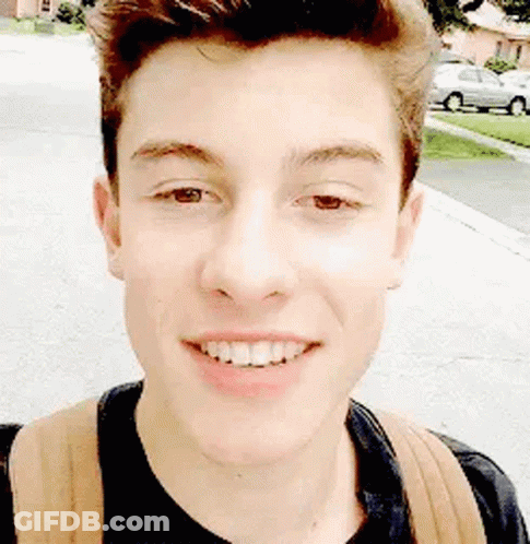 A Young Man With A Backpack Is Smiling For The Camera While Walking Down The Street . GIF