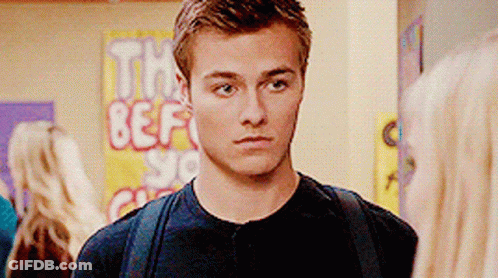 A Young Man With A Backpack Stands In Front Of A Sign That Says The Best GIF