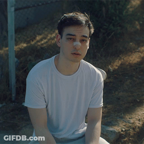A Young Man With A Bandage On His Nose Sits On The Ground GIF