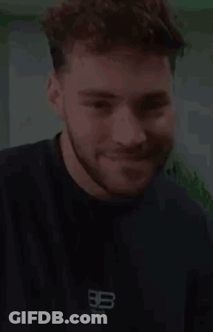 A Young Man With A Beard Is Smiling And Wearing A Black T-Shirt . GIF