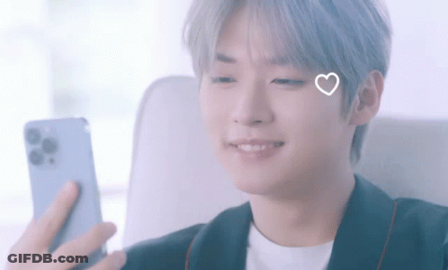 A Young Man With A Heart On His Face Is Looking At His Phone GIF