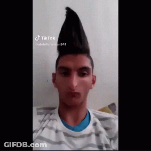 A Young Man With A Mohawk Hairstyle Is Wearing A Striped Shirt And Looking At The Camera . GIF
