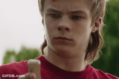 A Young Man With A Mullet Is Holding A Cell Phone . GIF