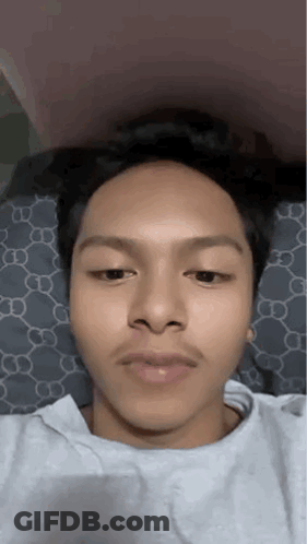A Young Man With A Mustache Is Laying On A Bed And Making A Funny Face . GIF