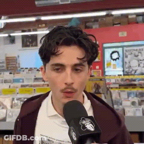 A Young Man With A Mustache Is Talking Into A Microphone . GIF