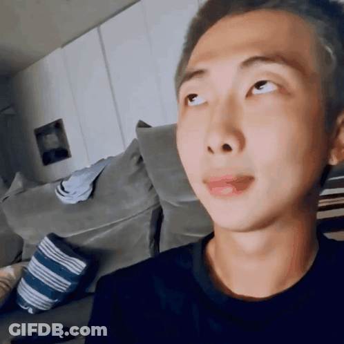 A Young Man With A Shaved Head Is Sitting On A Couch Looking Up At Something . GIF