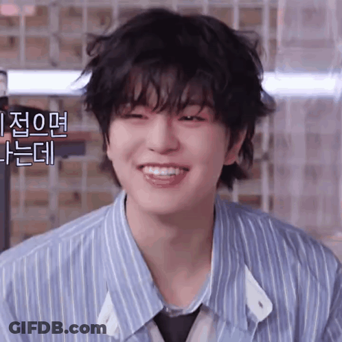 A Young Man With A Striped Shirt And Tie Is Smiling And Looking At The Camera . GIF