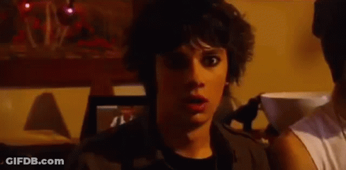A Young Man With A Surprised Look On His Face Is Standing In A Dark Room . GIF