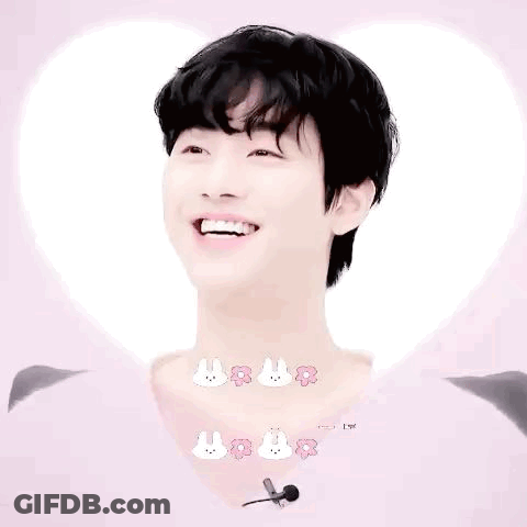 A Young Man With Black Hair Is Smiling In Front Of A Heart . GIF