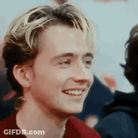 A Young Man With Blonde Hair And A Red Shirt Is Smiling And Looking At The Camera . GIF