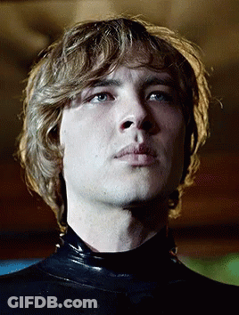 A Young Man With Blonde Hair And Blue Eyes Is Wearing A Black Latex Bodysuit GIF