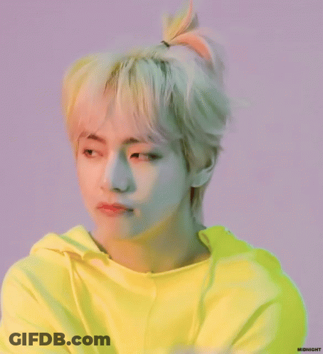 A Young Man With Blonde Hair In A Ponytail Is Wearing A Bright Yellow Hoodie . GIF