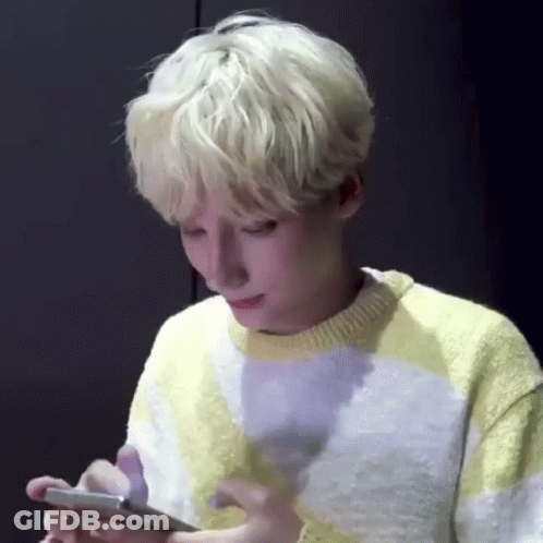 A Young Man With Blonde Hair Is Looking At His Cell Phone . GIF