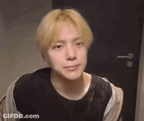 A Young Man With Blonde Hair Is Looking At The Camera In A Room . GIF