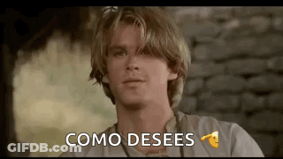 A Young Man With Blonde Hair Is Sitting In Front Of A Brick Wall And Saying `` Como Desees '' . GIF