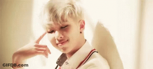 A Young Man With Blonde Hair Is Sitting In Front Of A Window With His Hand On His Head . GIF