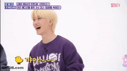 A Young Man With Blonde Hair Is Smiling And Holding A Duck In Front Of A Screen That Says Idol League GIF