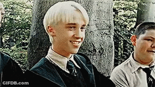 A Young Man With Blonde Hair Is Smiling While Standing Next To A Group Of Young Men . GIF