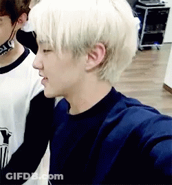 A Young Man With Blonde Hair Is Standing Next To Another Young Man In A Room . GIF