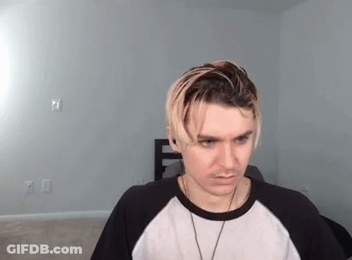 A Young Man With Blonde Hair Is Wearing A Black And White Shirt And A Necklace . GIF