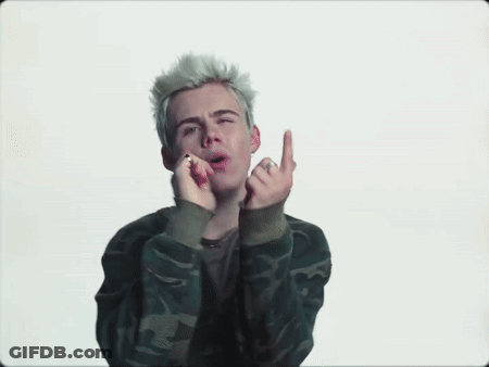 A Young Man With Blonde Hair Is Wearing A Camouflage Jacket And Giving The Middle Finger . GIF