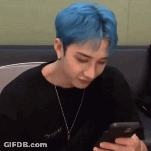 A Young Man With Blue Hair Is Looking At His Phone . GIF