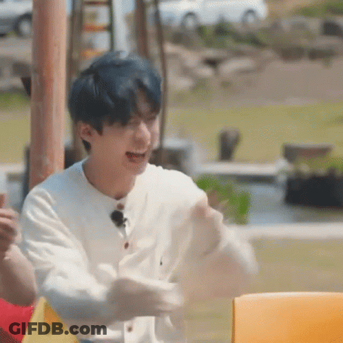 A Young Man With Blue Hair Is Sitting At A Table With His Arms Outstretched And Laughing . GIF