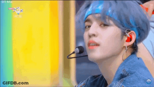A Young Man With Blue Hair Is Wearing A Headband And Earphones While Singing Into A Microphone . GIF