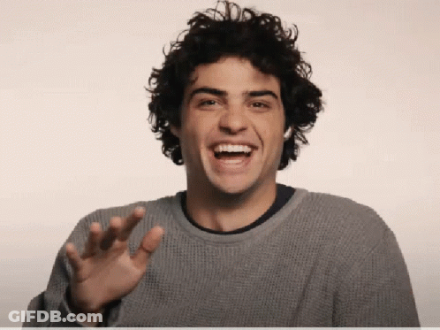A Young Man With Curly Hair Is Laughing And Waving His Hand GIF