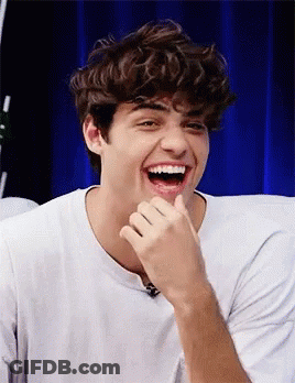 A Young Man With Curly Hair Is Laughing With His Hand On His Face . GIF