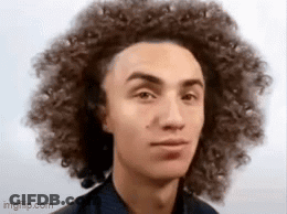 A Young Man With Curly Hair Is Looking At The Camera And Making A Funny Face . GIF