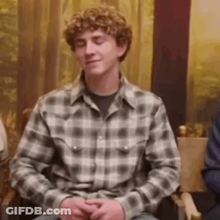 A Young Man With Curly Hair Is Sitting In A Chair With His Eyes Closed . GIF