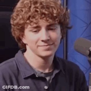 A Young Man With Curly Hair Is Sitting In Front Of A Microphone . GIF