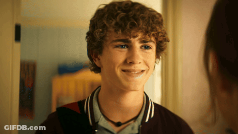 A Young Man With Curly Hair Is Smiling And Looking At Another Person GIF