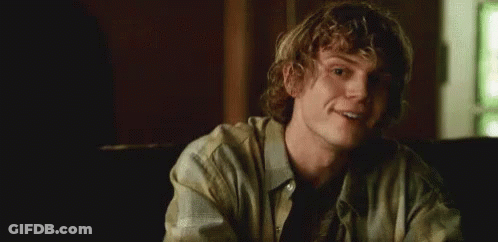 A Young Man With Curly Hair Is Smiling In A Dark Room . GIF
