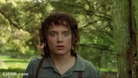 A Young Man With Curly Hair Is Standing In A Forest Looking At The Camera GIF