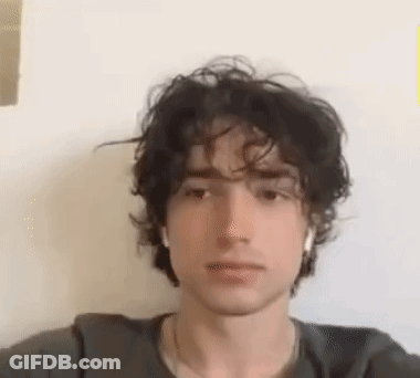 A Young Man With Curly Hair Is Taking A Selfie With A White Wall In The Background . GIF