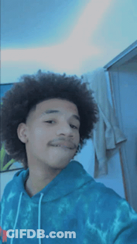 A Young Man With Curly Hair Is Wearing A Blue Tie Dye Sweatshirt GIF