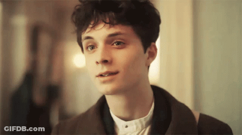 A Young Man With Curly Hair Is Wearing A Brown Jacket And A White Shirt GIF