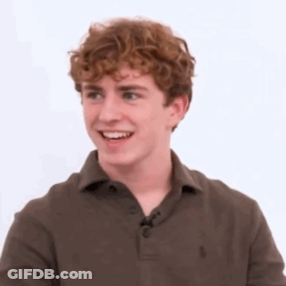 A Young Man With Curly Hair Is Wearing A Brown Polo Shirt And Smiling . GIF