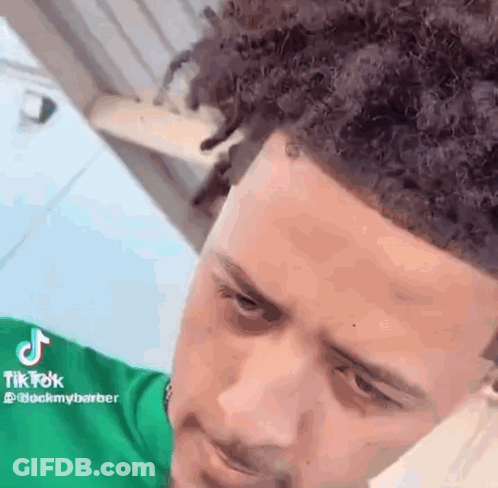 A Young Man With Curly Hair Is Wearing A Green Shirt And Looking Down . GIF