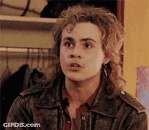 A Young Man With Curly Hair Is Wearing A Leather Jacket And Earrings . GIF