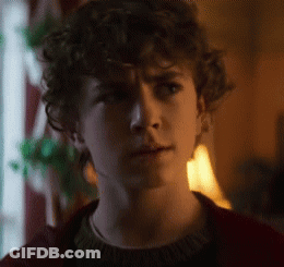 A Young Man With Curly Hair Is Wearing A Red Sweater . GIF