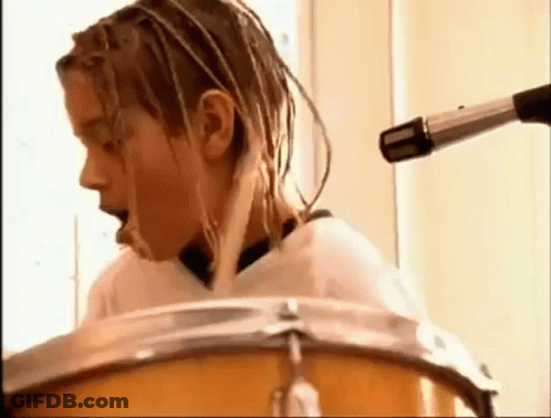 A Young Man With Dreadlocks Is Playing Drums In Front Of A Microphone . GIF