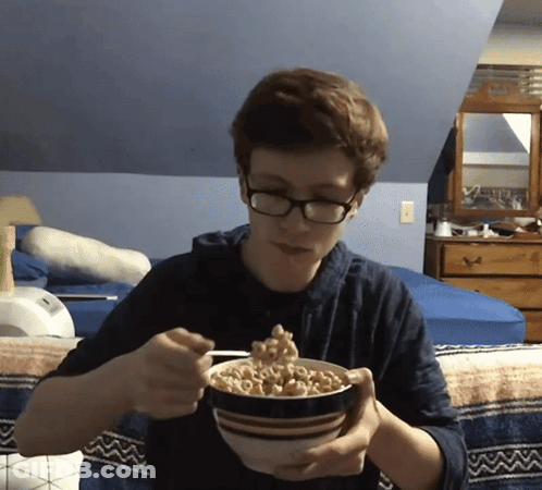 A Young Man With Glasses Is Eating Cereal From A Bowl GIF